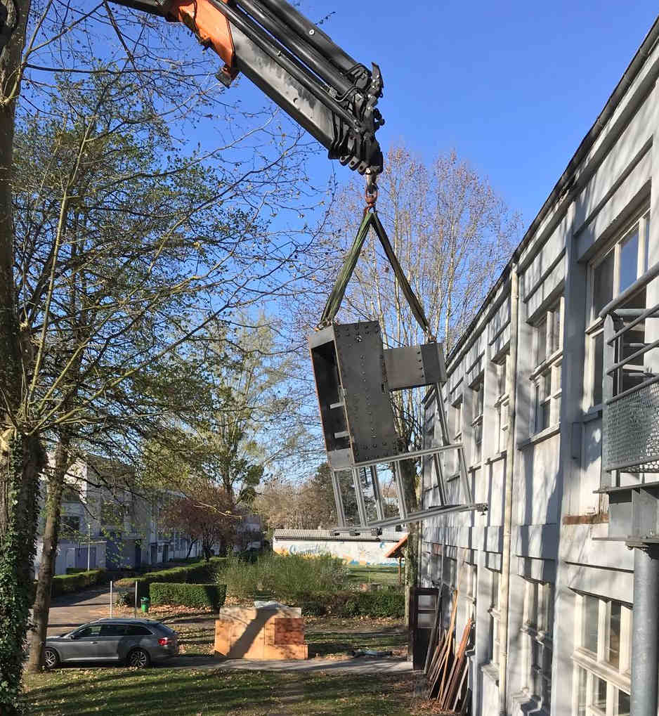 Photo d'une machine suspendue au bout d'un bras mécanique devant un bâtiment